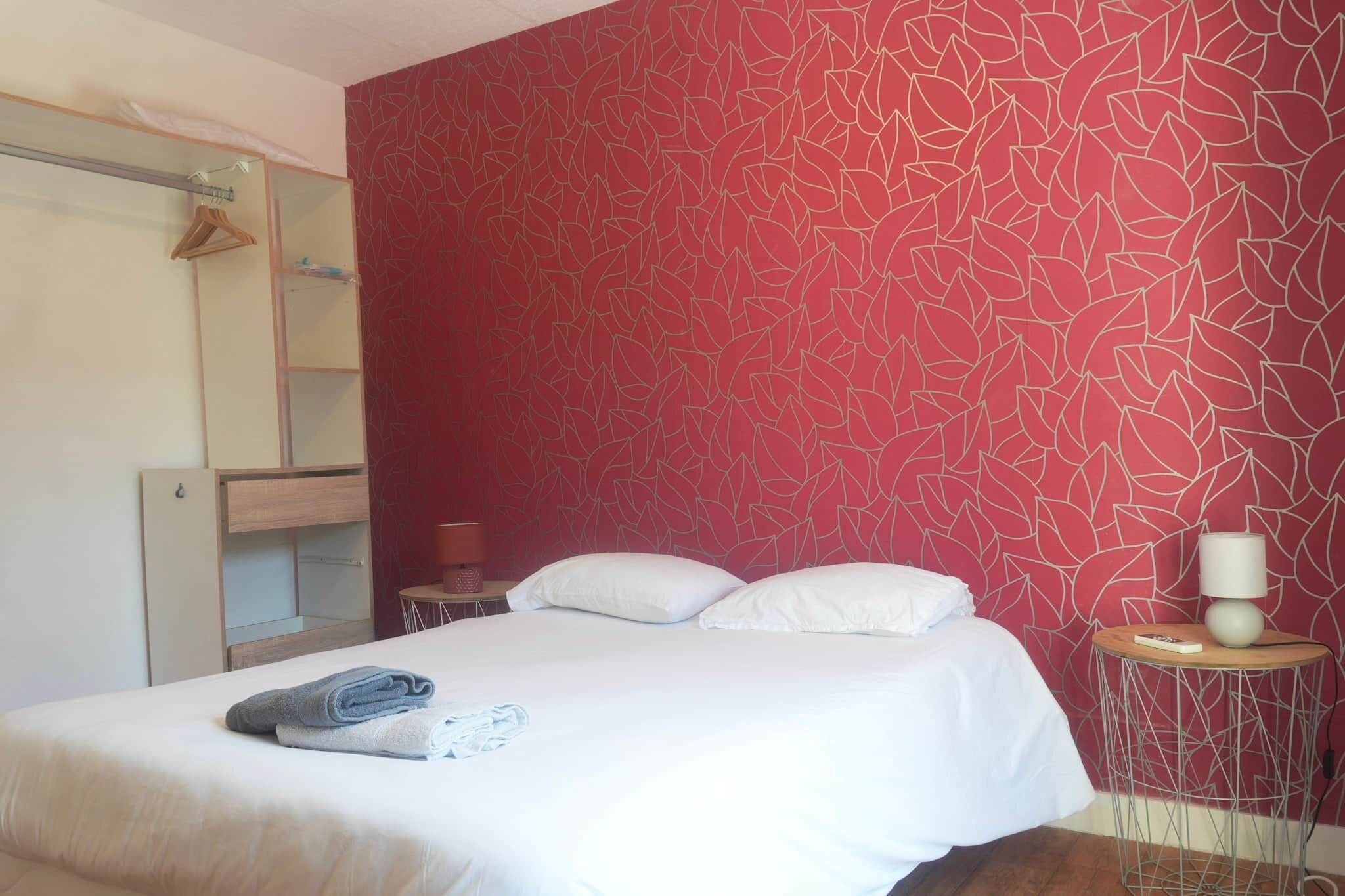 A hotel room with a bed, pillows, a bedside table with a lamp, a mirror, and a wardrobe.