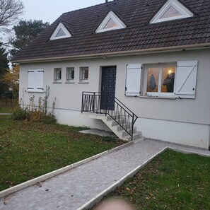 A two-story house with a tiled roof, a front door, and a small front porch with a railing.