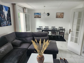 A modern living room with a sectional sofa, a dining table with chairs, and artwork on the walls.