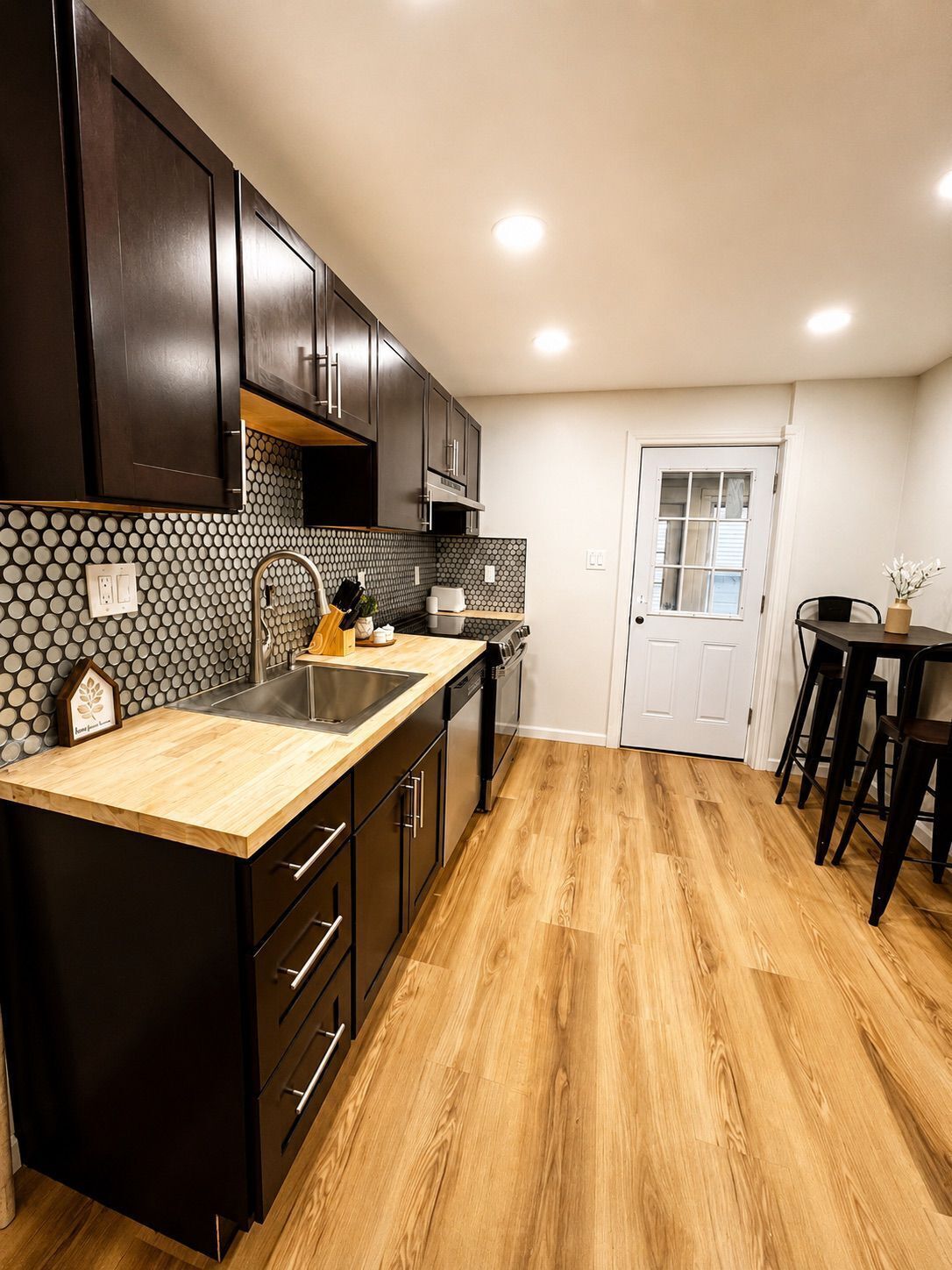 A kitchen with dark cabinets, a wooden countertop, a sink, and a dining area with chairs.