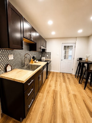 A kitchen with dark cabinets, a wooden countertop, a sink, and a dining area with chairs.