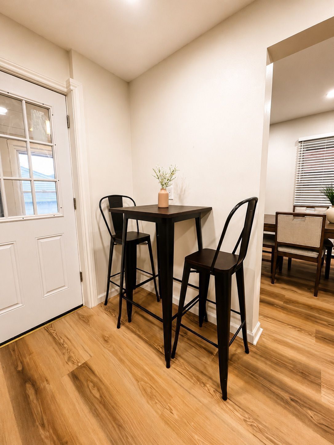 A dining area with a table and chairs, a vase with a plant, and a window with blinds.
