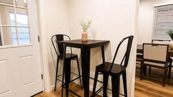 A dining area with a table and chairs, a vase with a plant, and a window with blinds.
