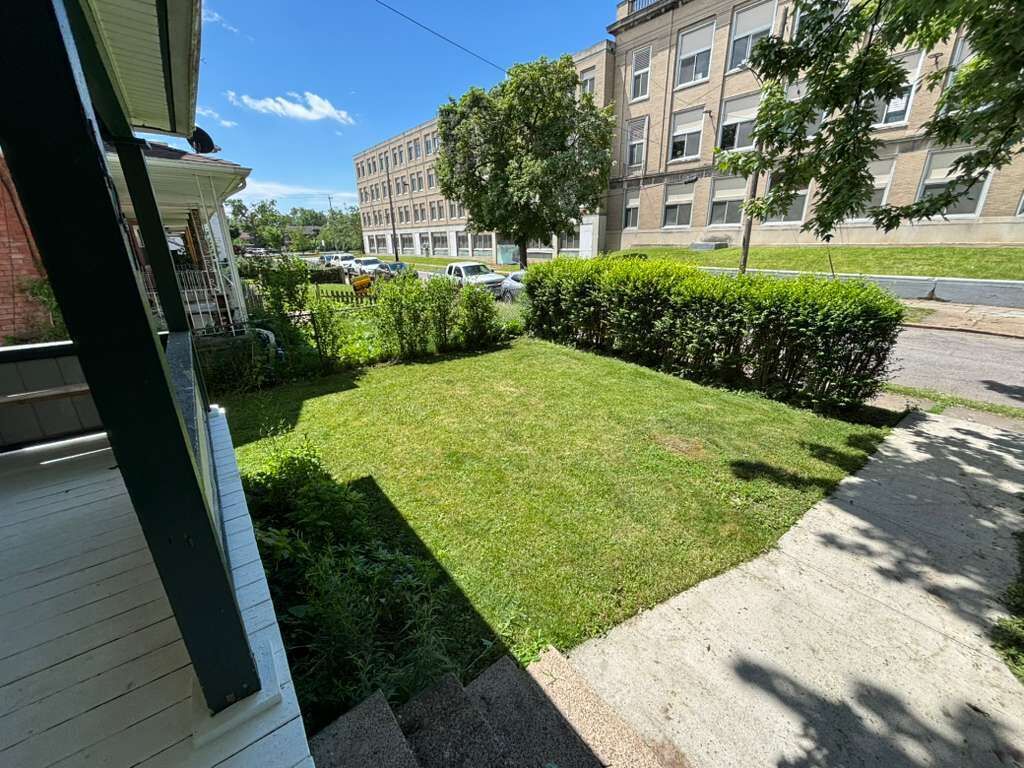 A residential area with a well-maintained lawn, a sidewalk, and a multi-story building in the background.