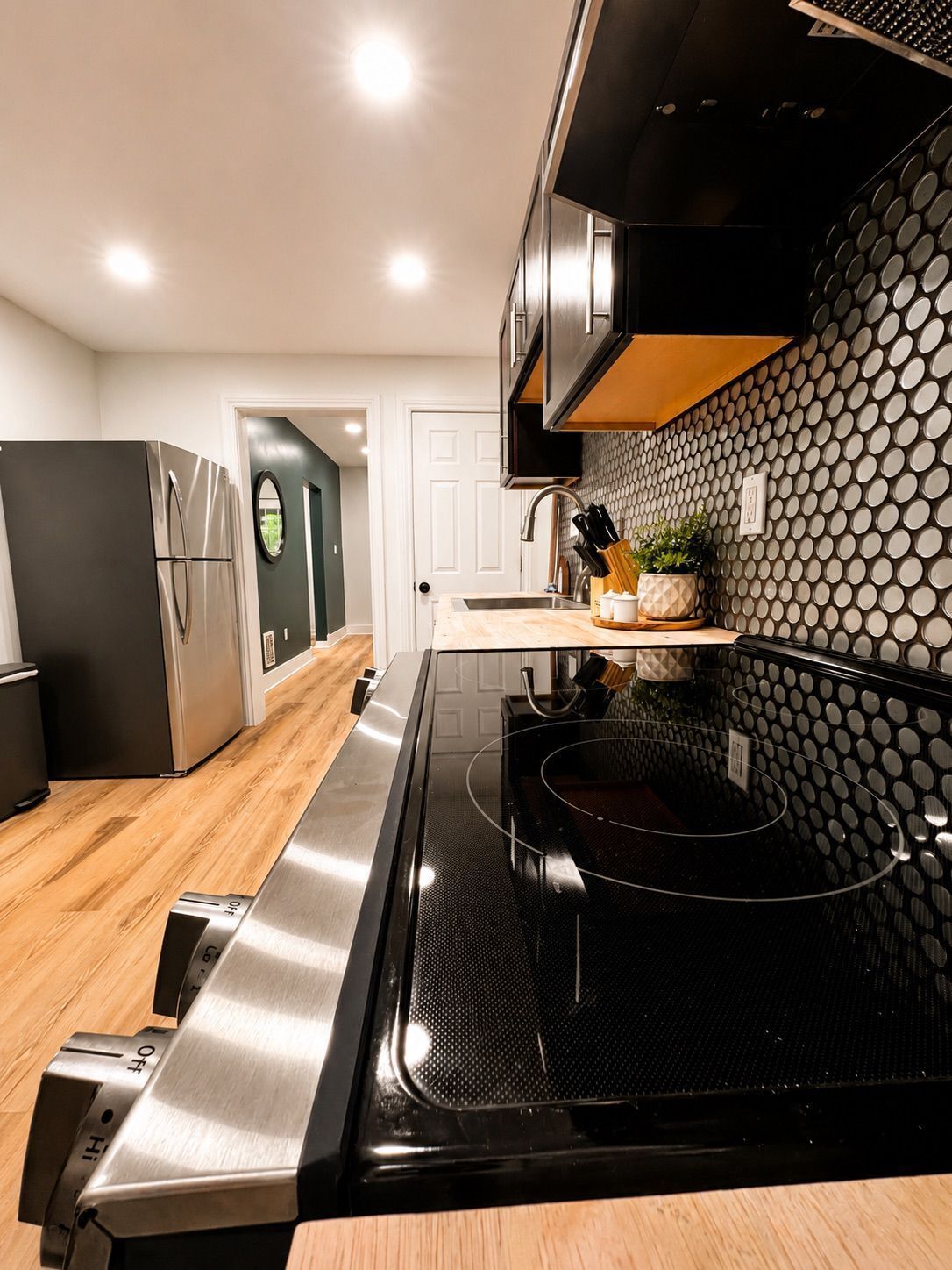 A modern kitchen with a black stove, stainless steel appliances, and a wooden floor.