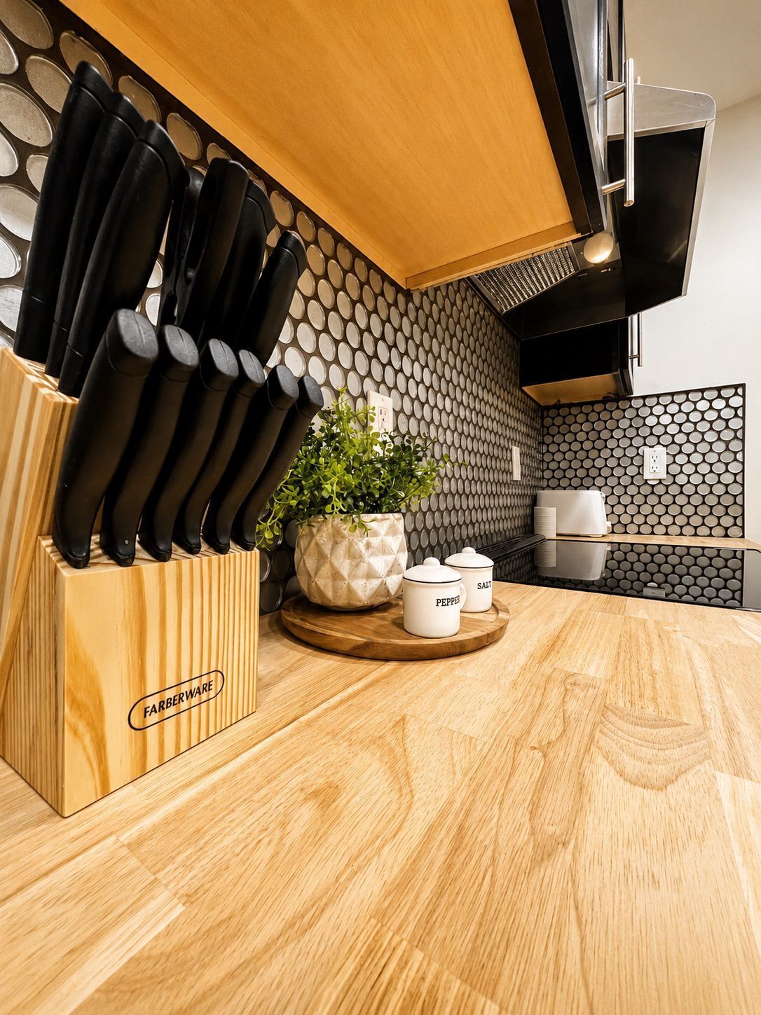 A kitchen with a knife block, a potted plant, and salt and pepper shakers on a wooden countertop.