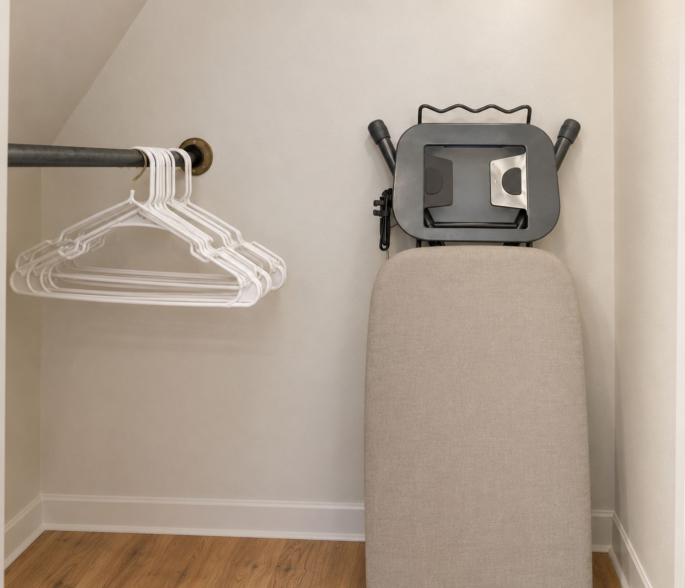 A corner of a room with a wooden floor, a white wall, a grey ironing board, and a white wall-mounted ironing board.