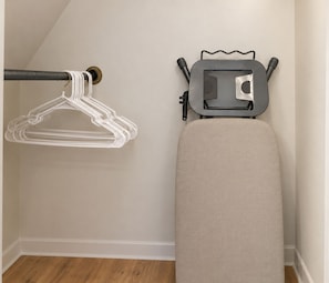 A corner of a room with a wooden floor, a white wall, a grey ironing board, and a white wall-mounted ironing board. - Niagara Fall NY Brand New Full 3BR 7 Sleep Fully Furnished (Niagara Falls)