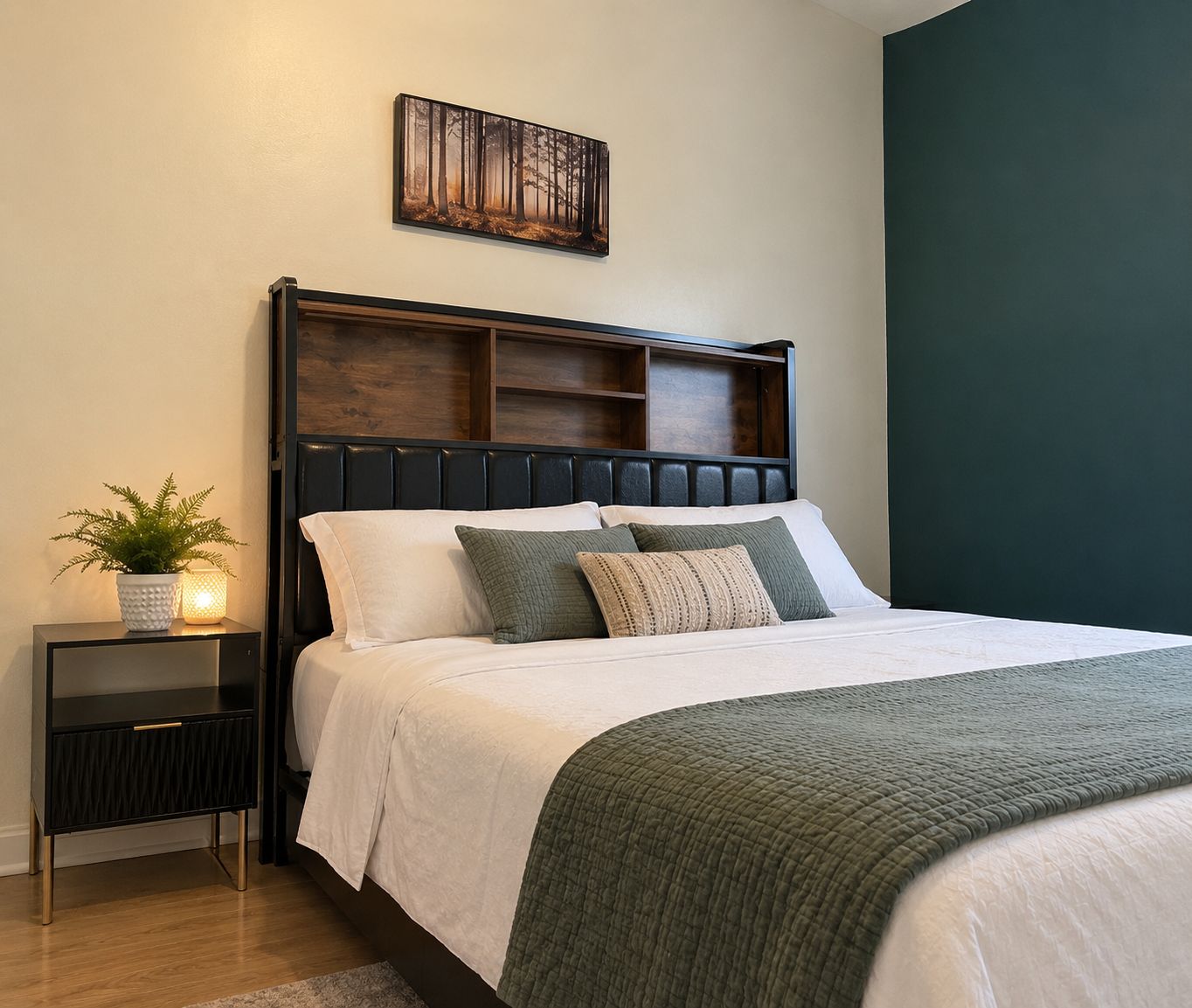 A bedroom with a bed, a nightstand, a potted plant, and a wall-mounted artwork.