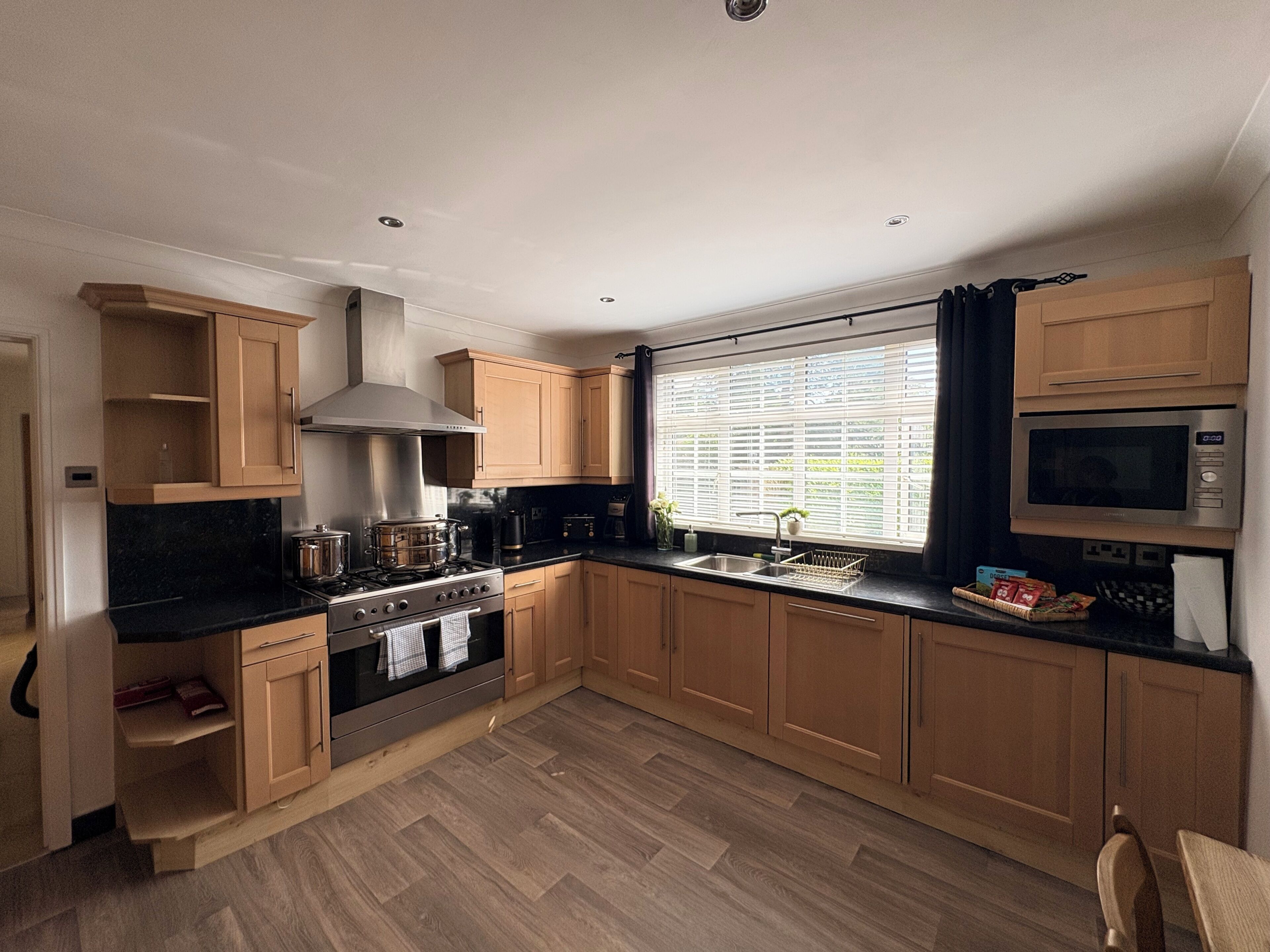 A modern kitchen with wooden cabinets, a stainless steel stove, and a window with blinds.