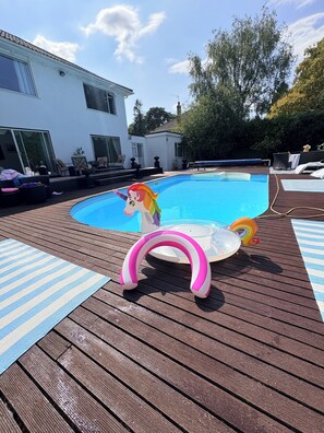An outdoor swimming pool with a wooden deck, lounge chairs, and a unicorn floatation device.