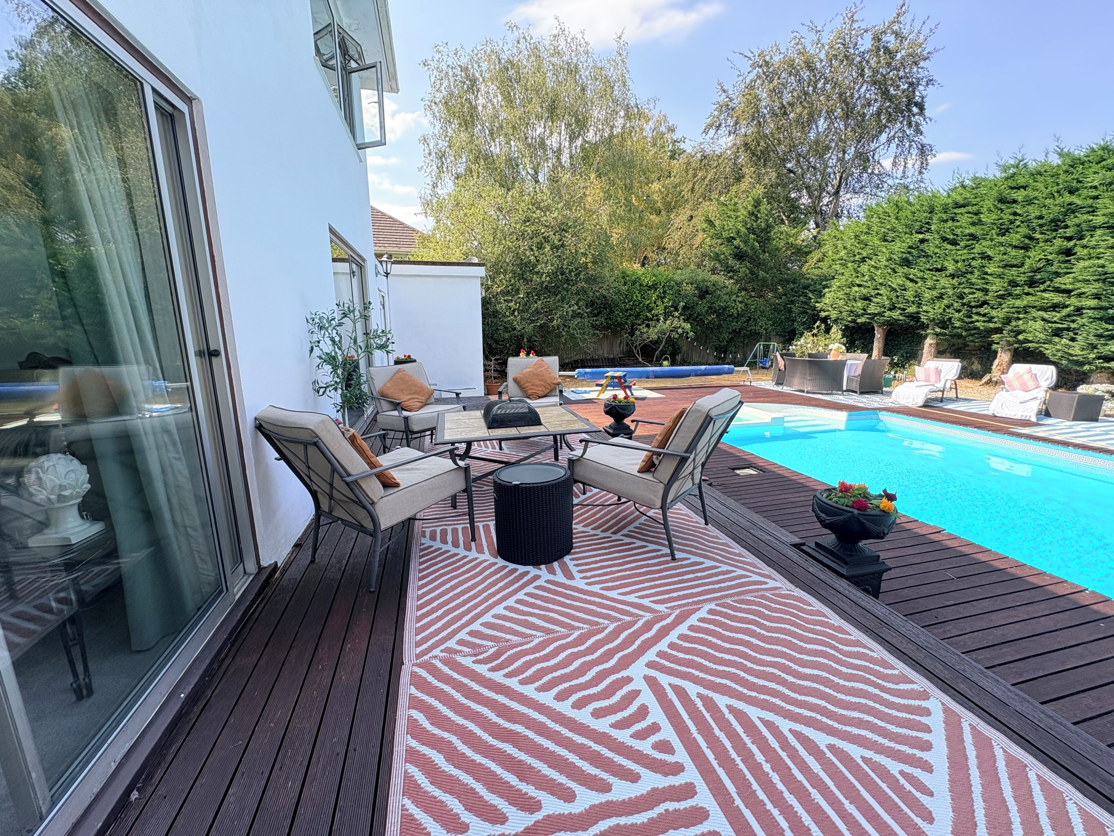 Ein Poolbereich mit Holzterrasse, Gartenmöbeln und Schwimmbecken.