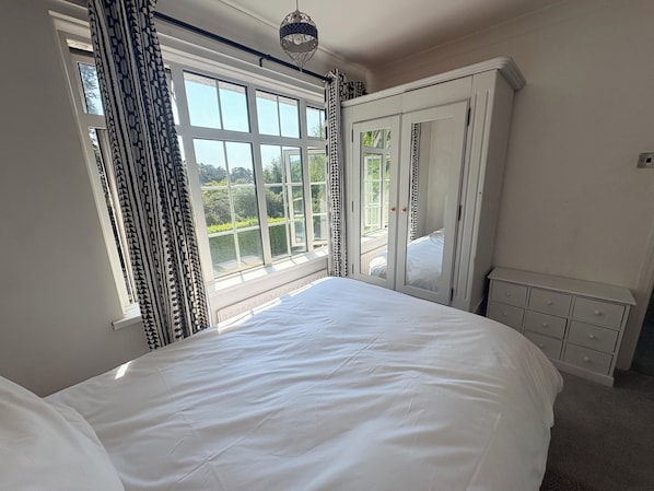 A bedroom with a large bed, a wardrobe, and a window with curtains.