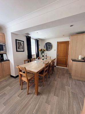 A dining area with a wooden table, chairs, a clock, and a microwave.