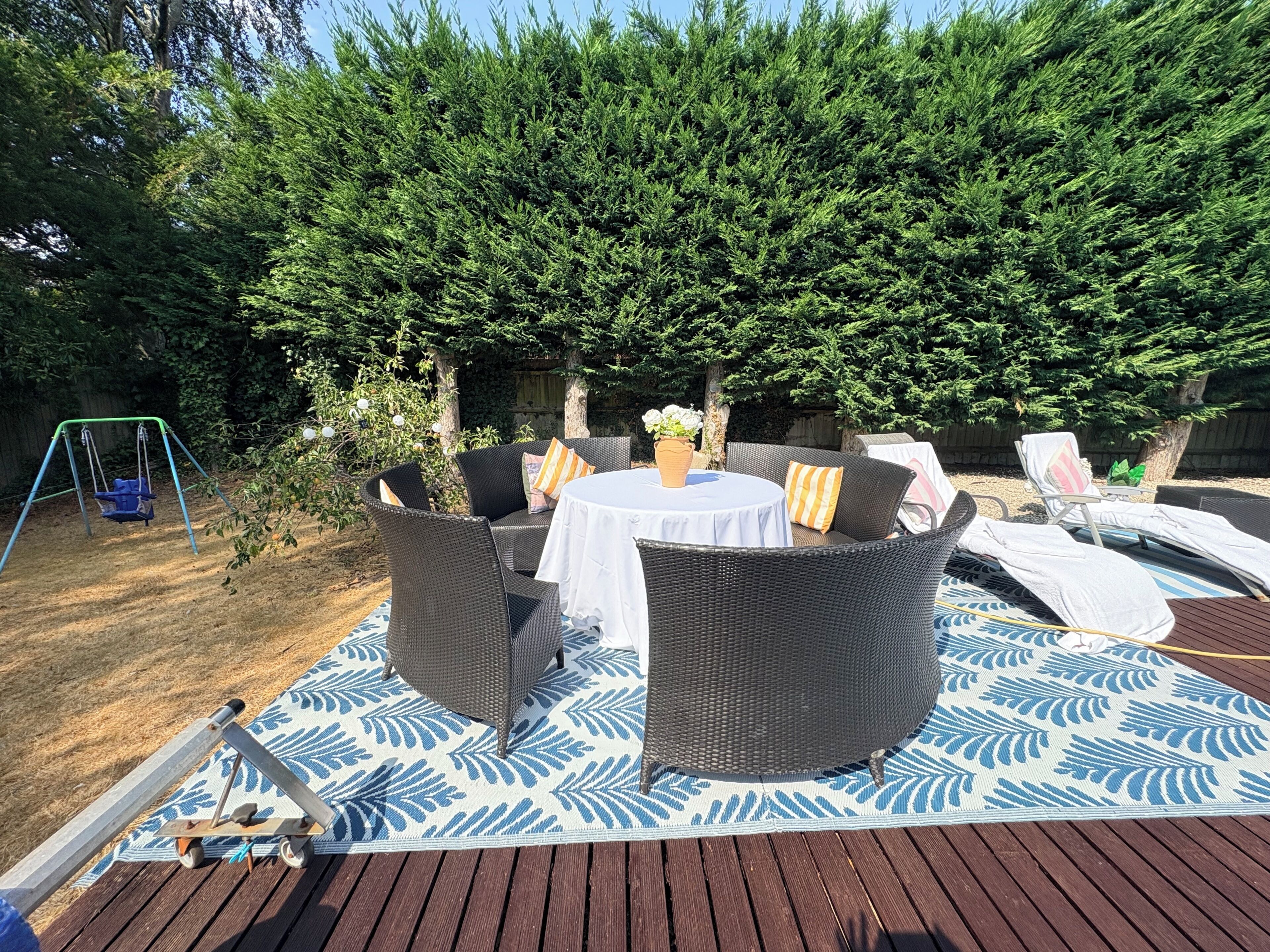 A patio with wicker furniture, a swing set, and a decorative rug.