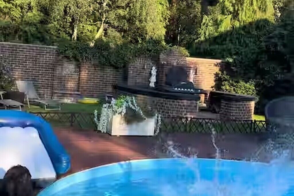 Ein Schwimmbecken mit Rutsche, umgeben von einer Ziegelmauer und viel Grün.