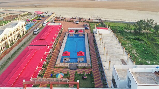 A resort with a swimming pool, red-roofed buildings, and a beach view.