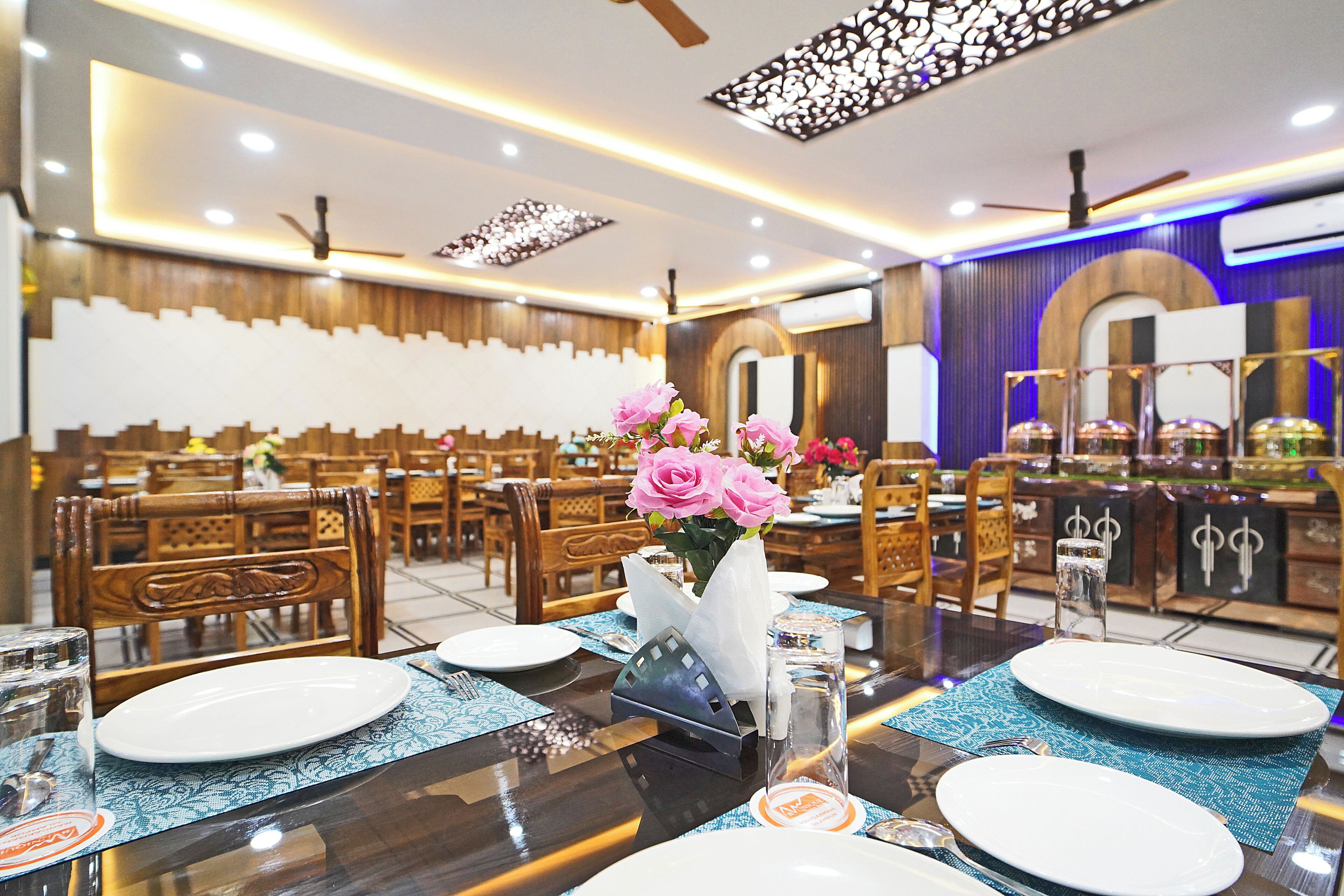Un restaurante con mobiliario de madera y una mesa central adornada con un jarrón de flores rosas.
