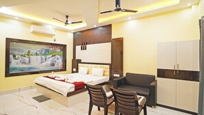 A modern bedroom with a bed, a desk, two chairs, a wardrobe, and a painting on the wall.