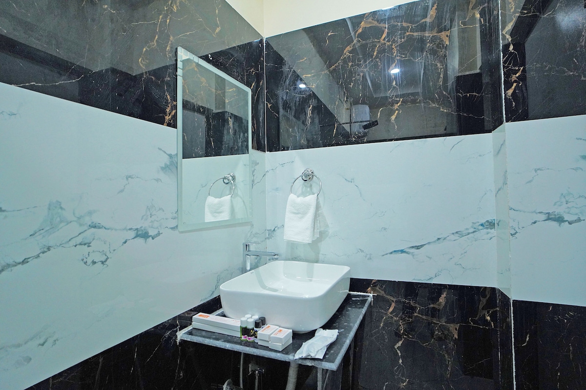 Un baño moderno con un espejo grande, un lavamanos blanco y paredes de mármol.