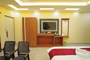 Habitación de hotel con cama, escritorio con televisor de pantalla plana, dos sillas, armario de madera y espejo.