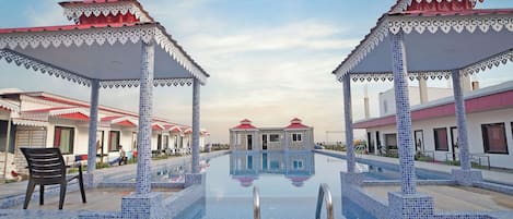 Una piscina con borde de azulejos, rodeada de zonas de estar cubiertas con techos rojos y detalles blancos.