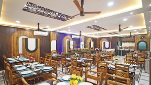 A restaurant with multiple dining tables, wooden chairs, ceiling fans, and decorative wall panels.
