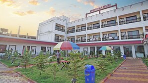 A multi-story building with balconies, a central courtyard with potted plants, and a sign reading 'Unique Beach Resort'.