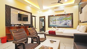 A hotel room with a bed, a TV, a painting, a desk with a book, and two chairs.