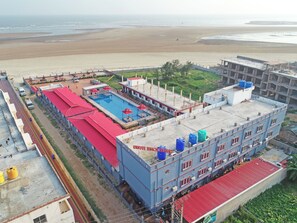 Un edificio con piscina, vista a la playa y una construcción con techo rojo.