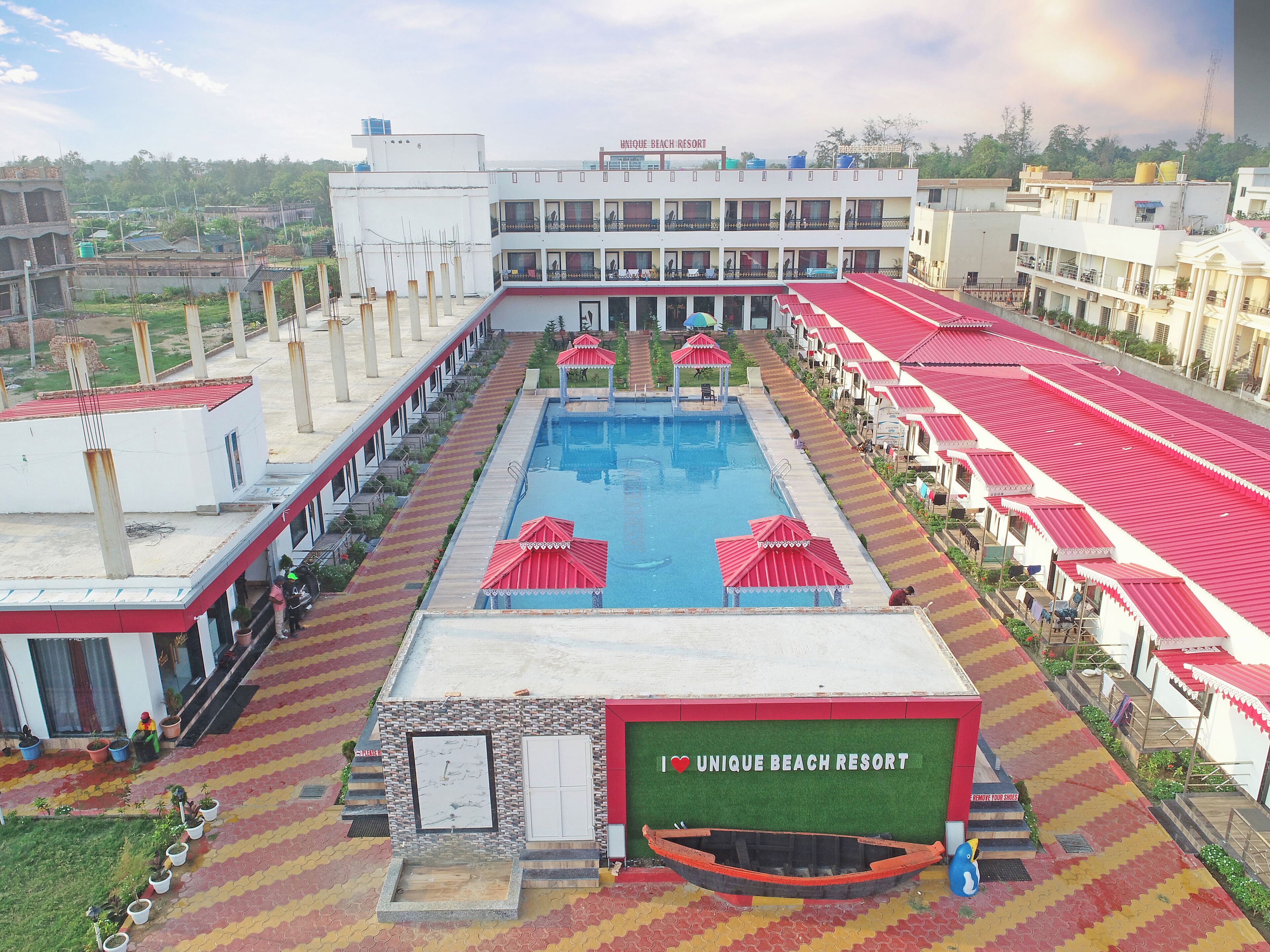Una piscina con sombrillas rojas, un cartel que dice 'I ♥ UNIQUE BEACH RESORT' y un bote frente a la piscina.