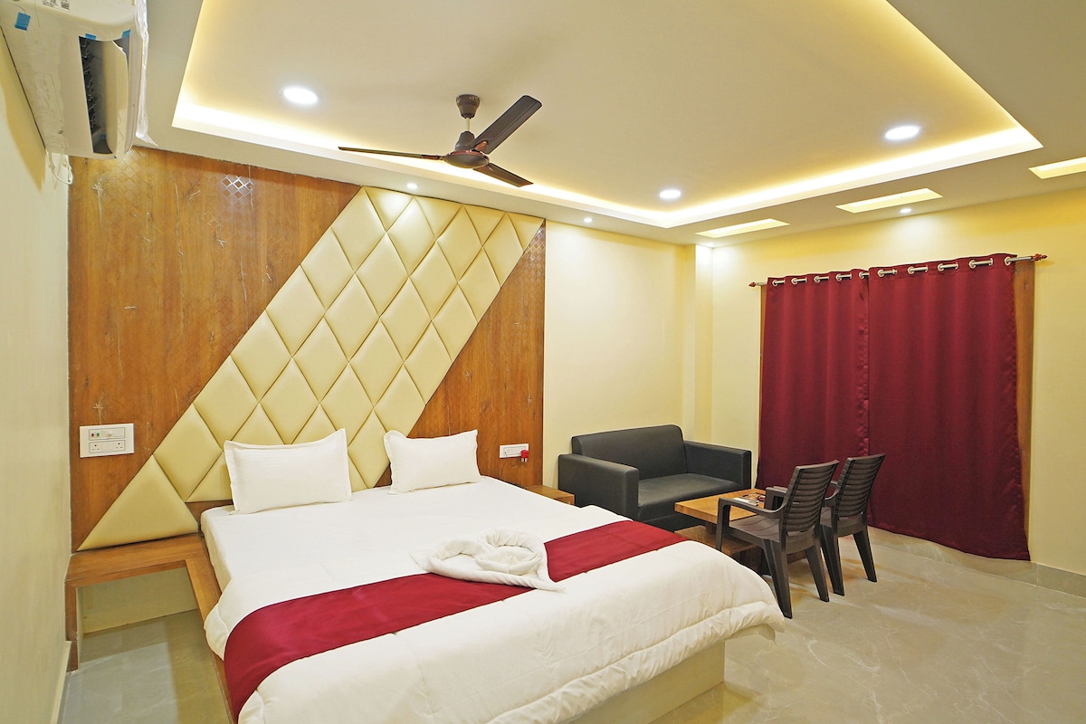 Habitación de hotel con cama, escritorio, silla, cortina roja y ventilador de techo.