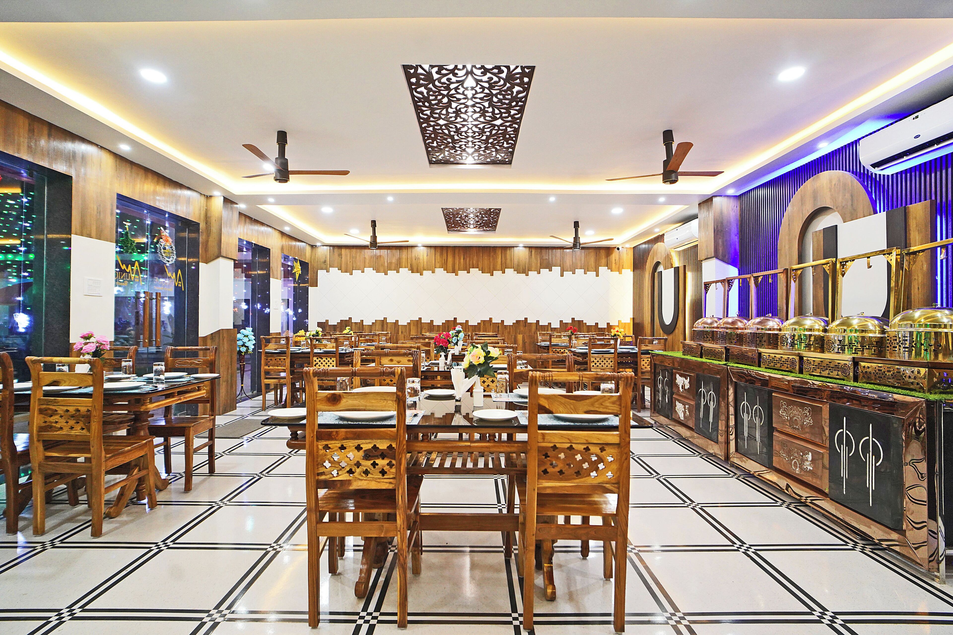 Un restaurant spacieux, doté de nombreuses tables et chaises, de ventilateurs de plafond et de panneaux décoratifs sur les murs.