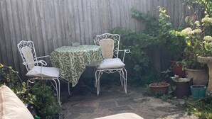 Een terras met een tafel en twee stoelen, omgeven door potplanten en een houten omheining.