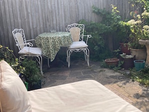 A patio with a table and two chairs, surrounded by potted plants and a wooden fence. - Seaford 1-bed House Sleeps 2, Sea Views & Parking (Seaford)