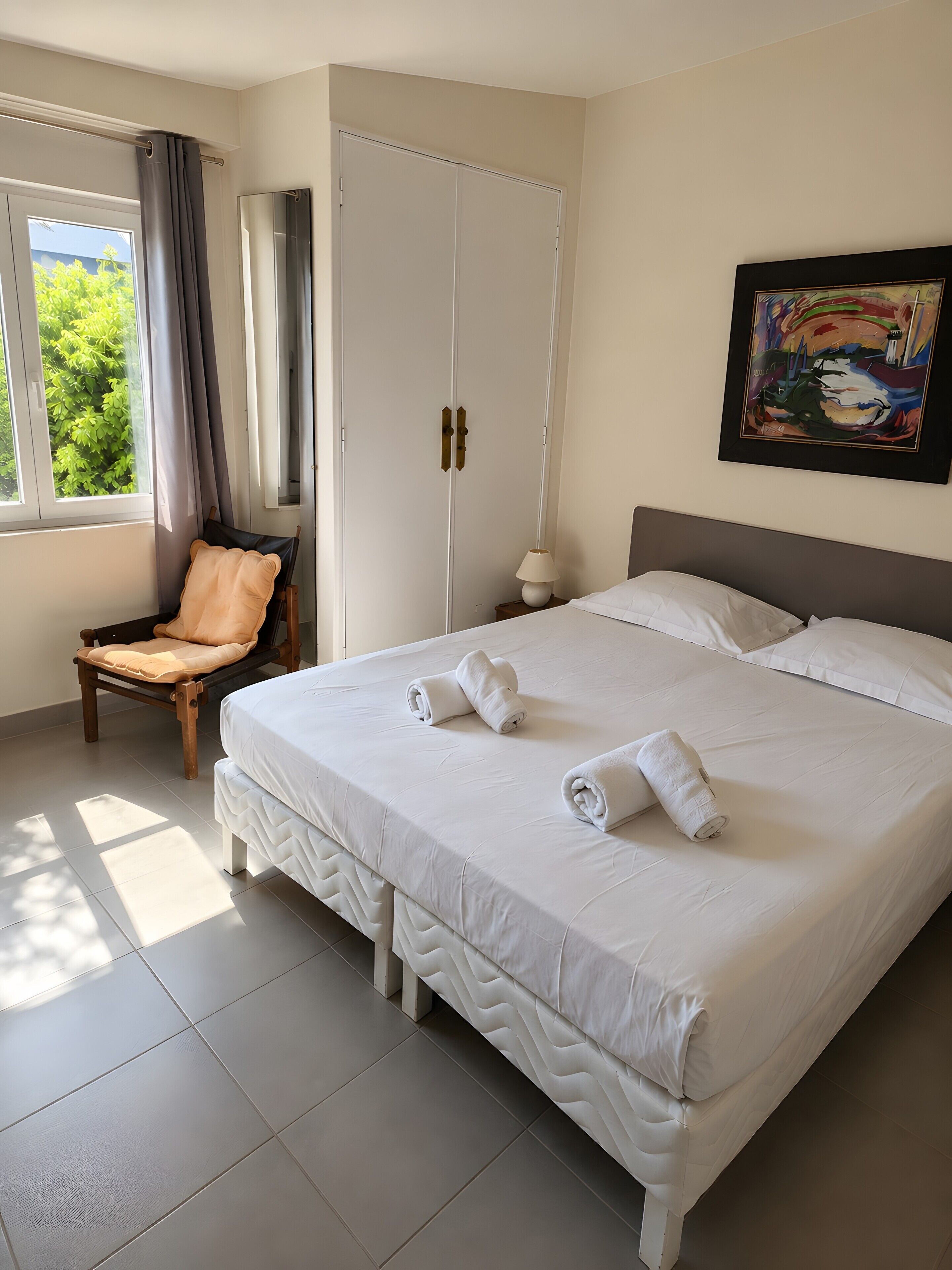 Une chambre d’hôtel avec un grand lit, une chaise, une armoire et un tableau au mur.