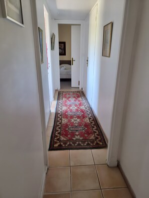 Ein Flur mit Teppichmuster, weißen Wänden und einem Bett im Hintergrund.