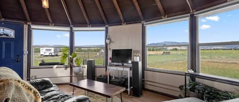 Amplia sala de estar con un gran ventanal, televisor y una mesa.