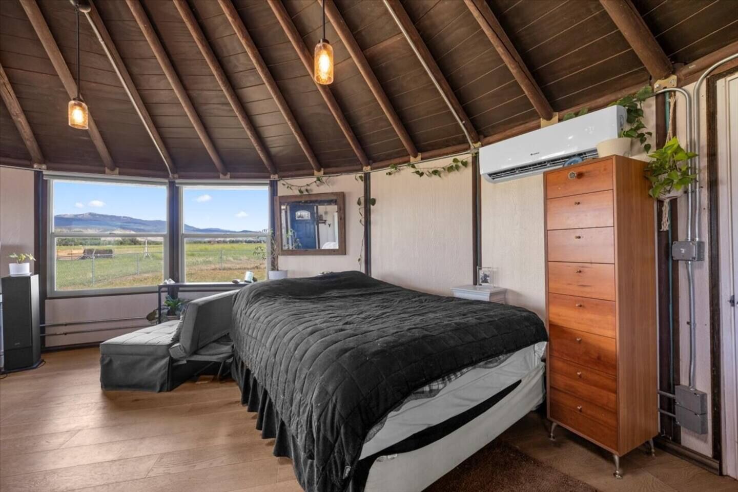 Une chambre à coucher comprenant un lit, une commode en bois, une fenêtre donnant sur l’extérieur et un plafond avec des poutres en bois.