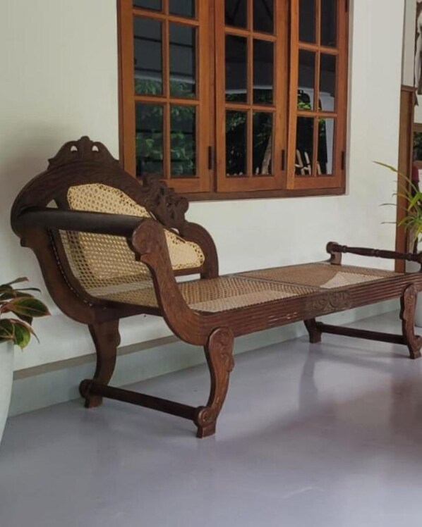 Un banco de madera con asiento y respaldo trenzados, ubicado frente a una ventana de madera.