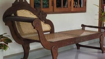 A wooden bench with a woven seat and backrest, positioned in front of a window with a wooden frame.