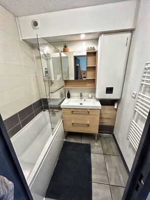 A modern bathroom with a bathtub, a sink, a mirror, and a towel rack.