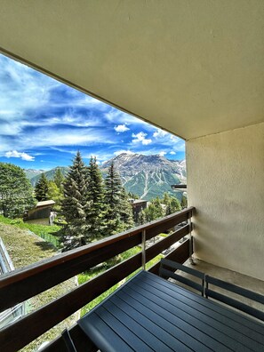 Un balcón con vistas a las montañas, un banco de madera y una mesa.