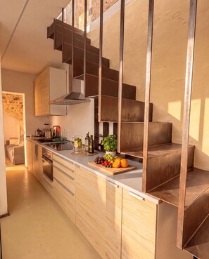 A modern kitchen with a central island, a built-in stove, and a wooden staircase. - Casa Mille e una Stella: Rooftop Terrace & Open-Sky-Room (Siracusa)