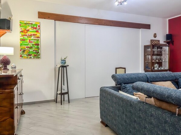 Una sala de estar con un sofá azul, un mueble de madera, un jarrón decorativo y una obra de arte en la pared.