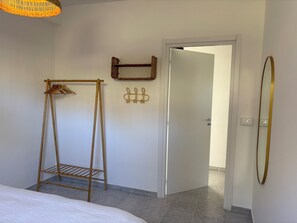 Una camera da letto con un letto, un appendiabiti in legno, un gancio per cappotti e una porta che dà su un'altra stanza.