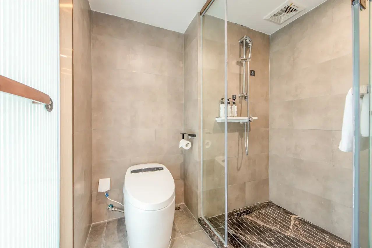 A modern bathroom with a glass-enclosed shower, a toilet, and a marble floor.