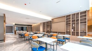 A modern dining area with multiple tables and chairs, a kitchen in the background, and built-in shelving units.