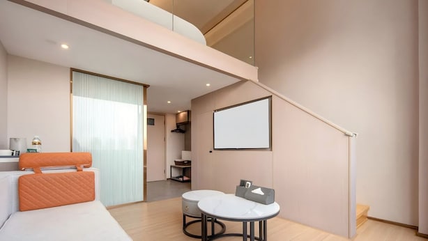 A modern hotel room with a bed, a small round table, a sofa, a staircase, and a large window.