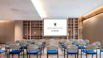 A conference room with rows of chairs, a large screen, and shelves with decorative items.